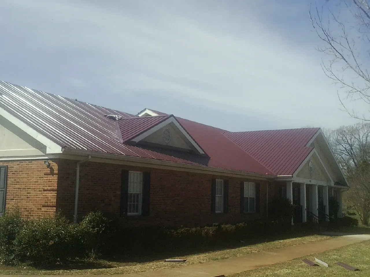 Red metal roof with gabled entries on a long brick building, from a Hail Damage Roof Repair job in North Beach