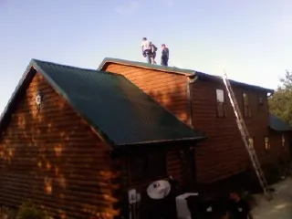 Crew on the ridge of a green metal roof on a two story log home in North Beach