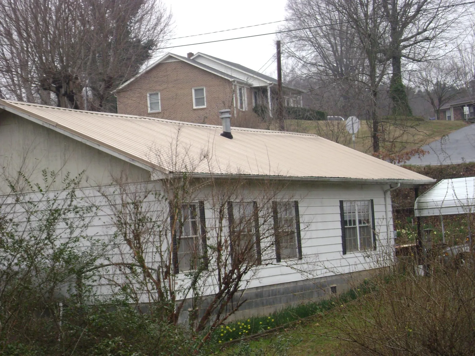 Tan metal roof on a white sided house set into a hillside — Commercial Roofing by Roofing Brothers in North Beach